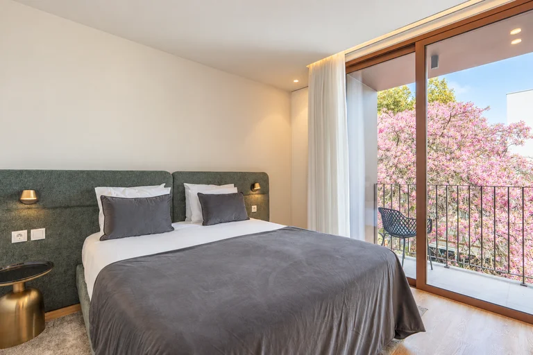Quarto com cabeceira verde e varanda junto às árvores em flor